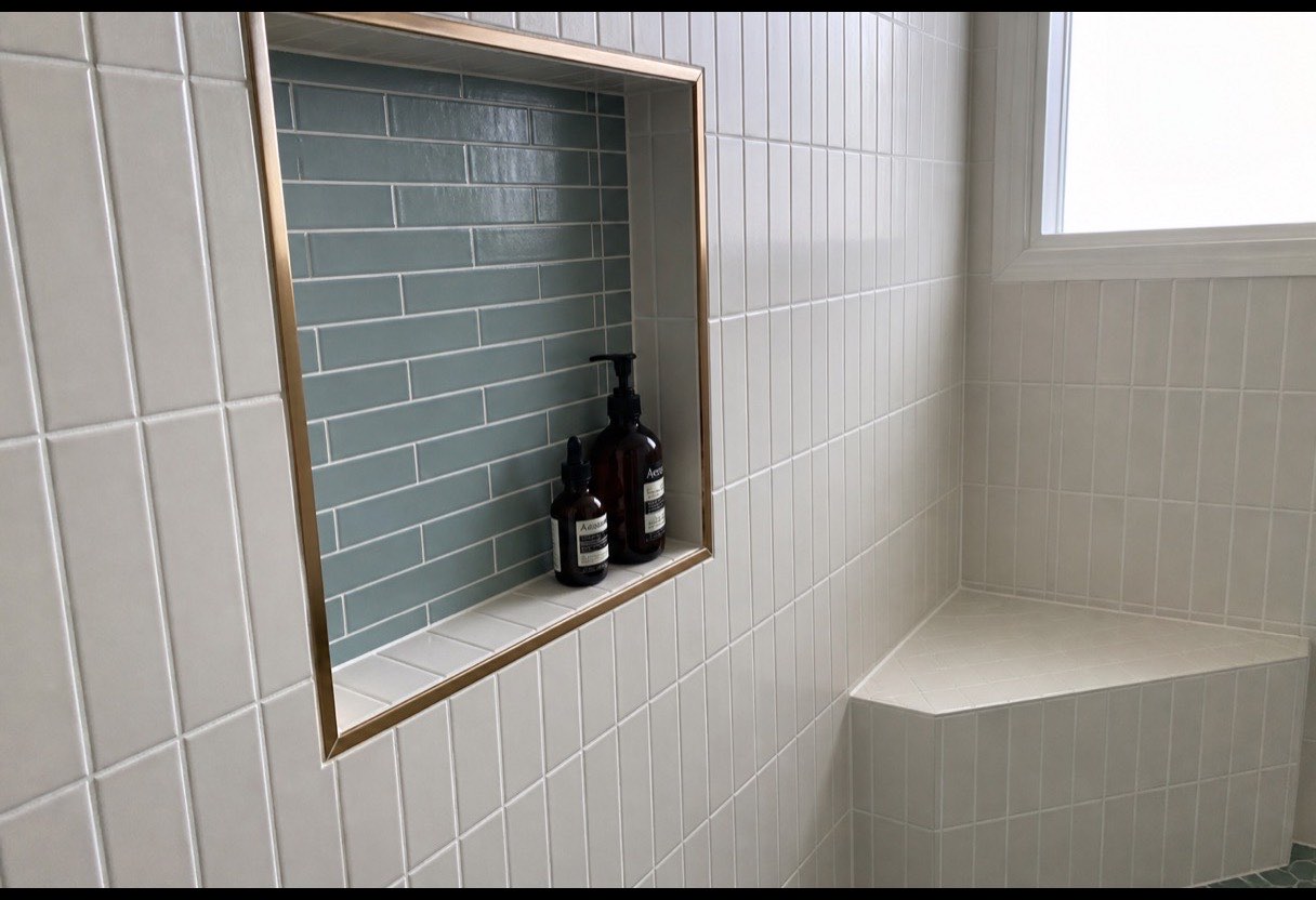 Recessed storage set within reach and a tiled bench. Both are decided at layout stage, not at the end.
